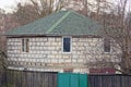 Part of a gray brick house with a green tiled roof with vegetation and trees behind a fence Royalty Free Stock Photo