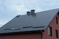 Part of a private house with a red wall under a brown tiled roof with metal chimneys against a background of gray sky Royalty Free Stock Photo