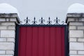 Part of a red metal door with black sharp rods and a brick fence under the snow Royalty Free Stock Photo