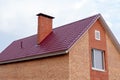 Part of a two-story private building of red brick against a clear sky. Fragment of a roof with a pipe and a window on the house. Royalty Free Stock Photo
