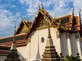 A part of the Wat Pho Temple with golden roof details with sun reflection, two small spires with shadows on the wall and a blue Royalty Free Stock Photo
