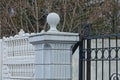 Part of a white concrete column with a stone ball in a black iron fence