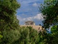 Parthenon on acropolis hill between green folliage, Athens Greece