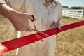 Partial female farmer cutting red ribbon on farm