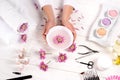 partial image of woman holding bath for nails over table with flowers, towels, colorful sea salt, aroma oil bottles, nail