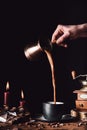 partial image of woman pouring coffee from turk into cup at table with chocolate, truffles, candles and coffee grains