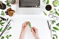 Partial top view of person holding green leaf at workplace with laptop, cup of coffee, green leaves and office supplies Royalty Free Stock Photo