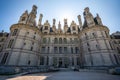 Dramatic view of Chateau Chambord with sunshine highlight behind in bright blue sky.