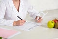 View of dietitian holding caliper and writing meal plan at workplace with fruits on table