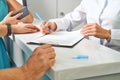 Partial view of doctor in white coat making notes in notepad with female patient near by during appointment in clinic Royalty Free Stock Photo