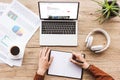 partial view of man making notes in notebook at workplace with laptop with airbnb website, papers, cup of coffee