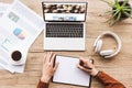 partial view of man working at laptop with depositphotos website, headphones, textbook, pen, infographics, coffee cup and potted