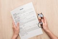 Partial view of recruiter holding resume template and glasses on wooden table.