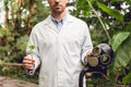 Partial view of scientist in white coat holding rubber gas mask and flask with plant sample in orangery. Royalty Free Stock Photo