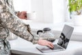 partial view of soldier holding cup of coffee and using laptop