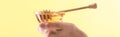 Partial view of woman holding glass bowl with honey and wooden dipper isolated on yellow, panoramic shot.