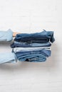 partial view of woman holding stack of blue denim clothes near white brick wall. Royalty Free Stock Photo