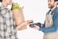 partial view of woman with paper package with food giving credit card to shop assistant with cardkey reader