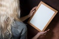 Partial view of young blond woman holding wooden frame, dark background, mockup Royalty Free Stock Photo