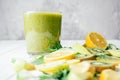 Partially blurred glass of green smoothie with green and yellow fruits and herbs cut into pieces on white table Royalty Free Stock Photo