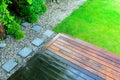 Partially cleaned wooden terrace with a pressure washer by the green lawn