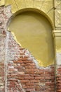 Partially destroyed plastered old brick wall with an arched niche and with fallen plaster. Ancient yellow brick wall
