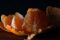 PARTIALLY PEELED MANDARIN WITH SEPARATED SEGMENTS ON A WOODEN BOARD