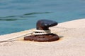 Partially rusted strong old iron mooring bollard screwed on local stone pier with five rusted metal bolts with white rope tied Royalty Free Stock Photo