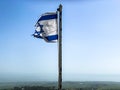 Partially torn israeli flag is waving in the wind on blue sky background