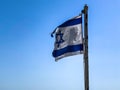 Partially torn israeli flag is waving in the wind on blue sky background