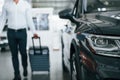 Partical view. Man in formal clothes is with luggage indoors near the car