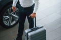 Partical view. Man in formal clothes is with luggage indoors near the car