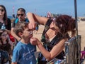 The participant of the Purim festival dressed in fabulous costume, puts a drawing on the boy`s face in Caesarea, Israel