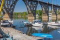 Participants of the local yacht-club anchorage near an arched bridge working with lifting sailboats to water