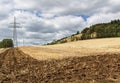 Partly ploughed field after the harvest with transmission tower and wooded hill in the background Royalty Free Stock Photo