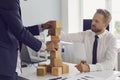 Partners building tower of wooden blocks on office table together developing strategy for business. Royalty Free Stock Photo