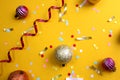 On a yellow background lies a swirling ribbon, festive confetti and balls