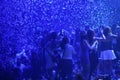 Party at disco with young people on the stage with blue lights and confetti rains.