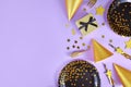 Party flat lay with black and golden plates, forks, gift, champagne bottle and star confetti on violet background