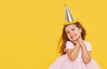 Party time. A joyful cute little child girl in a festive cap and elegant dress celebrates her birthday on a yellow Royalty Free Stock Photo