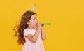 Party time. A joyful little girl in a festive cap and elegant dress celebrates her birthday. Blowing a whistle Royalty Free Stock Photo