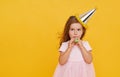 Party time. A joyful little girl in a festive cap and elegant dress celebrates her birthday. Blowing a whistle