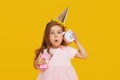 Party time. A joyful little girl in a festive cap and elegant dress celebrates her birthday. Holds a small alarm clock Royalty Free Stock Photo