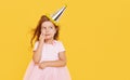 Party time. A joyful little girl in a festive cap and elegant dress celebrates her birthday. Pensive child is waiting Royalty Free Stock Photo