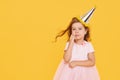 Party time. A joyful little girl in a festive cap and elegant dress celebrates her birthday. Pensive child is waiting for the holi Royalty Free Stock Photo