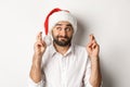 Party, winter holidays and celebration concept. Happy man in santa hat making christmas wish, cross fingers for good Royalty Free Stock Photo