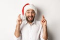 Party, winter holidays and celebration concept. Happy man in santa hat making christmas wish, cross fingers for good Royalty Free Stock Photo