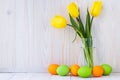 Paschal greeting card, mockup with text space. Festive easter frame with colorful eggs and bouquet of yellow tulips on light wood