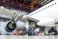 Passenger aircraft on maintenance of engine and fuselage repair in airport hangar. Rear view, under the wing.