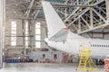 Passenger aircraft on maintenance of engine and fuselage repair in airport hangar, tail view Royalty Free Stock Photo